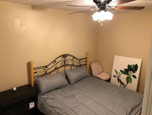 Ein Schlafzimmer mit Bett, Nachttisch, Deckenventilator und einem an der Wand hängenden Gemälde.