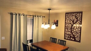 A dining area with a wooden table and chairs, a chandelier, a window with blinds, and a decorative wall panel. - Great PRIVATE Family T-Home! Easy Access City & Mountains! (Layton)