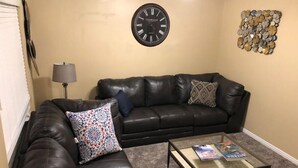 A living room with a black leather couch, a glass coffee table, a wall clock, and a decorative wall piece. - Great PRIVATE Family T-Home! Easy Access City & Mountains! (Layton)