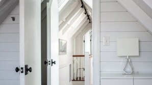 Un couloir étroit, doté d’un plancher en bois et de murs blancs, qui mène à un escalier avec une rampe en bois.