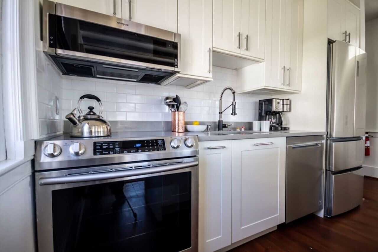 A modern kitchen with white cabinets, stainless steel appliances, and a kettle on the stove.