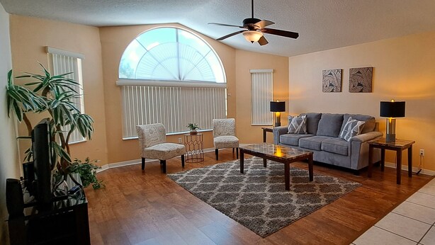 A living room with a sofa, two armchairs, a coffee table, a ceiling fan, and a large window. - Poolside Days & Disney Nights! Spacious Family Friendly 3BR/2BA Condo (Kissimmee)