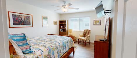 A bedroom with a bed, a chair, a desk, a bookshelf, and a TV mounted on the wall.