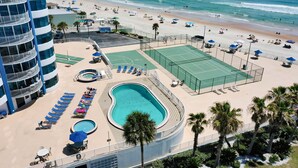 Un hotel con piscina, canchas de tenis y vista al mar.