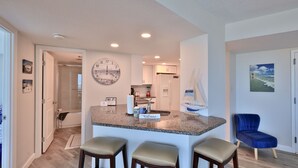 Una cocina moderna con una isla central, taburetes de bar, un reloj y una decoración con un velero.