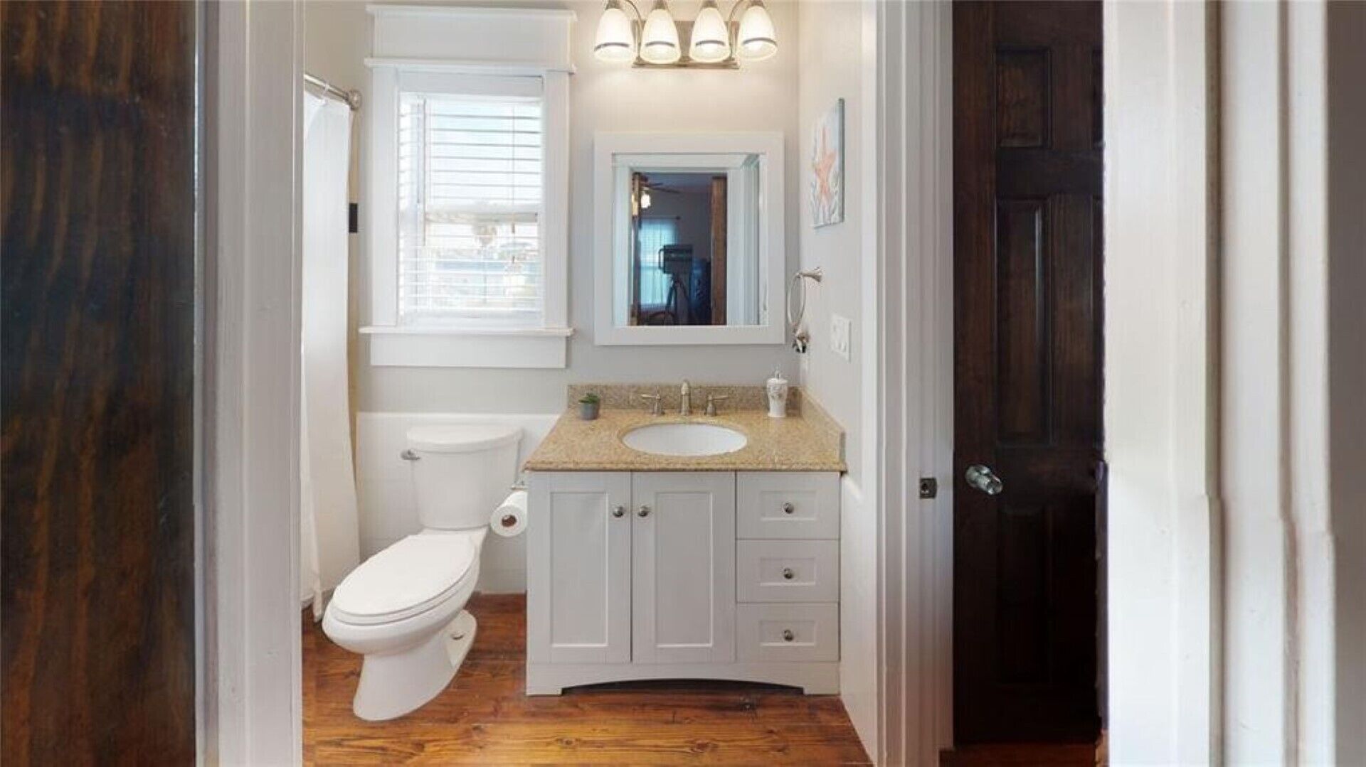A bathroom with a toilet, sink, vanity, and a mirror.