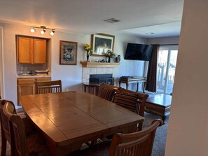 Un coin repas avec une table et des chaises en bois, une cheminée, une cuisine avec des placards en bois et un téléviseur fixé au mur.