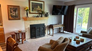 A living room with a fireplace, a television, and a dining area with a table and chairs. - Rum River Retreat! Clean & Cozy on 15 acres! (Cambridge)