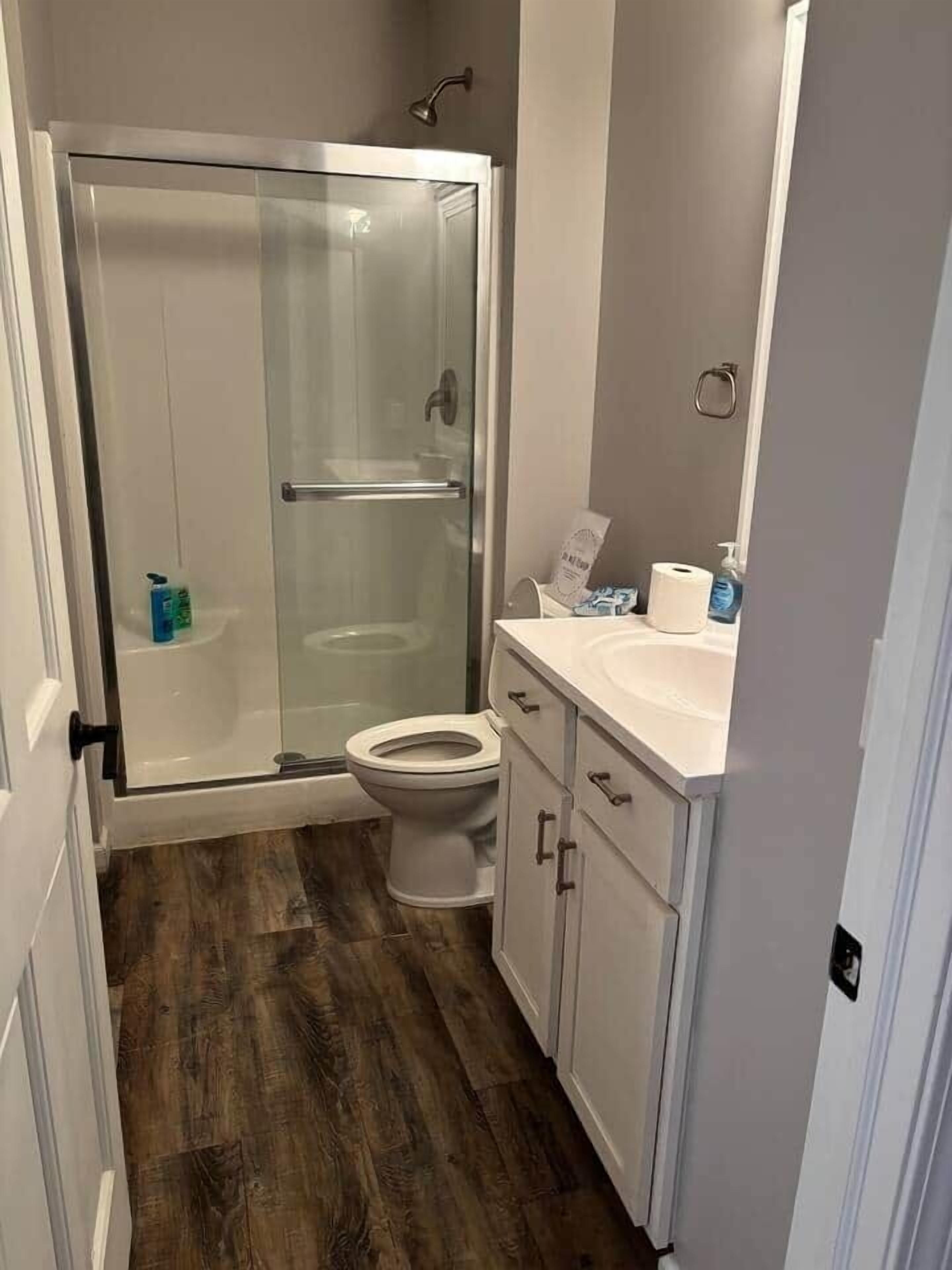A bathroom with a glass-enclosed shower, a toilet, and a sink with cabinets.