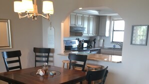 Zona pranzo con tavolo e sedie in legno, un lampadario e una cucina sullo sfondo.