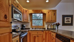 A kitchen with wooden cabinets, a built-in oven, a dishwasher, and a window with a view of trees. - Riverview Hideaway by Mountain Oasis | Dog-Friendly Riverview Cabin in Coosawattee (Ellijay)
