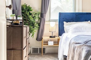 A bedroom with a bed, a bedside table with a lamp, a plant, and a dresser. - Spacious 4 BR/2 BA – 4 Min Walk to DT Ferndale! (Ferndale)