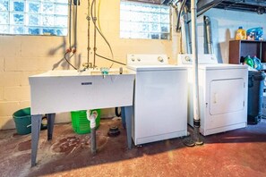 Een wasserette met een wasmachine, droger en een wastafel met leidingen.