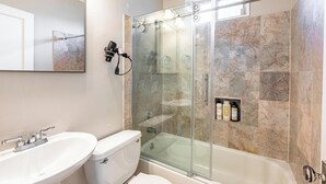 Un baño moderno con ducha de vidrio, lavamanos blanco y retrete.