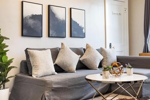 A modern living room with a grey sofa, three framed artworks, a small round table, and a potted plant. - Spacious 4 BR/2 BA – 4 Min Walk to DT Ferndale! (Ferndale)