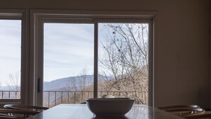 Ein Essbereich mit großem Tisch und Stühlen, einer Schüssel in der Mitte und Blick auf Berge durch große Fenster.
