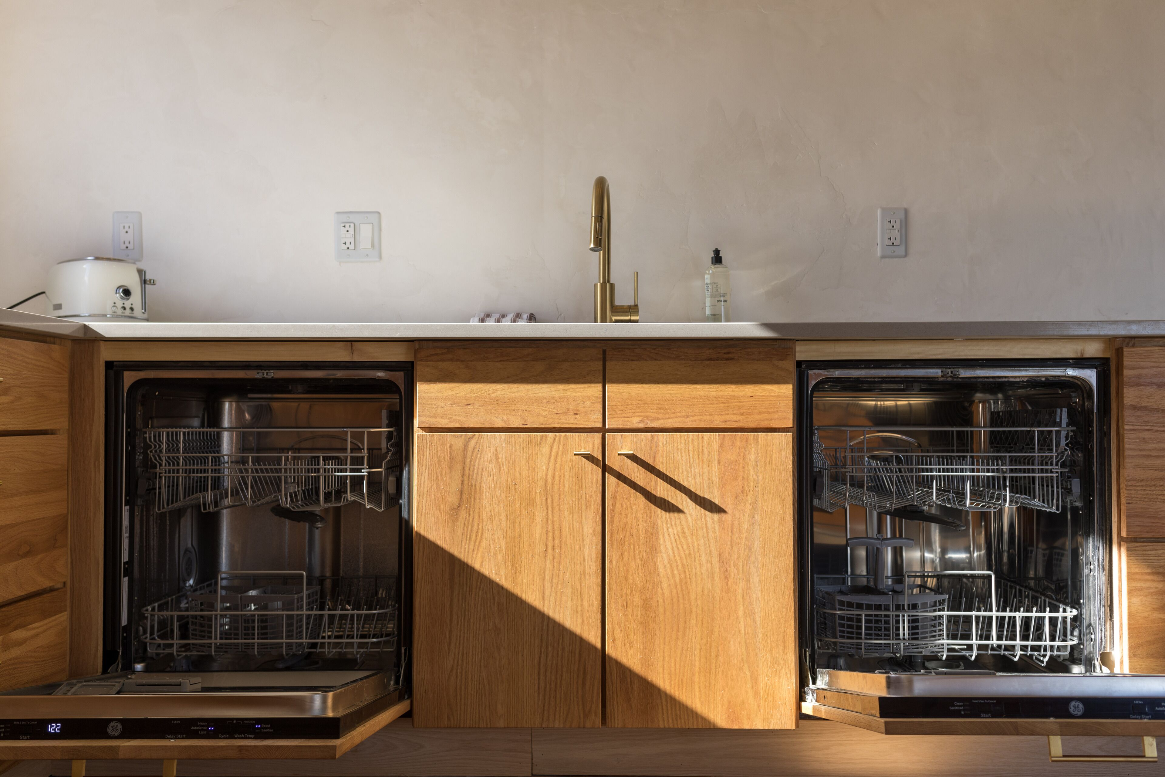Eine Küche mit zwei eingebauten Geschirrspülern, Holzschränken und einer Arbeitsplatte mit Toaster und einer Flasche Spülmittel.