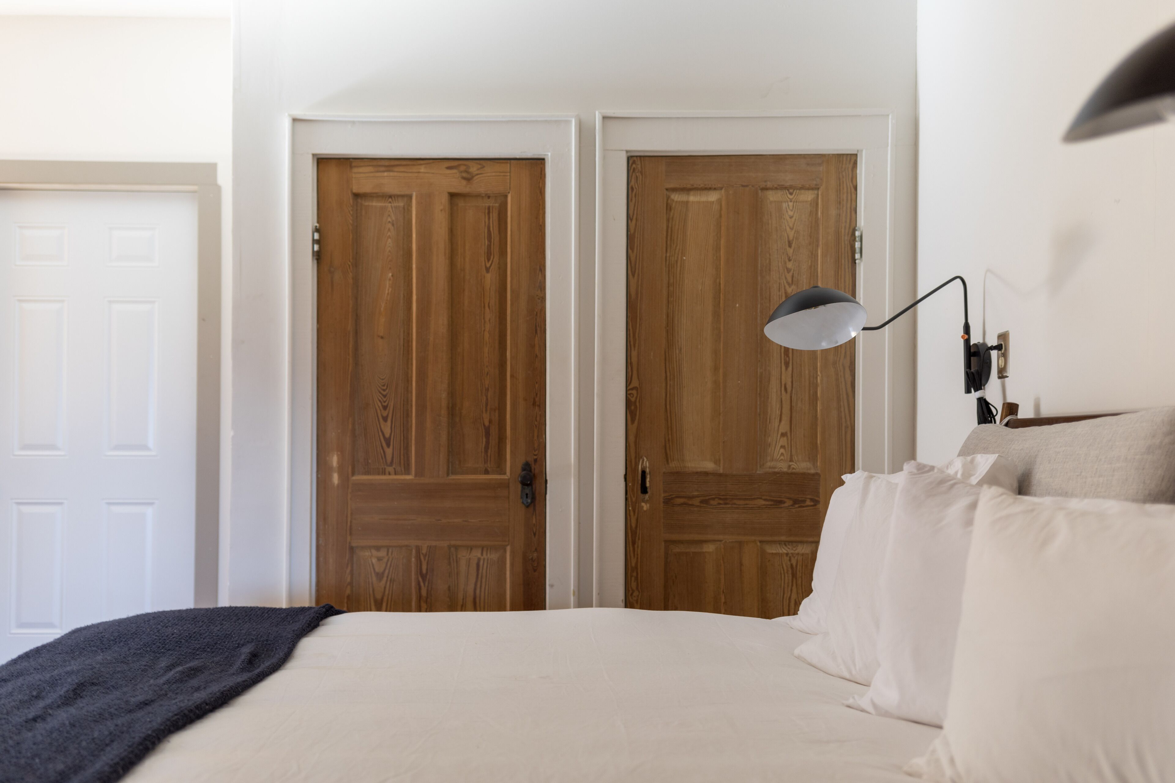 A bedroom with a bed, white walls, wooden doors, and a bedside lamp.