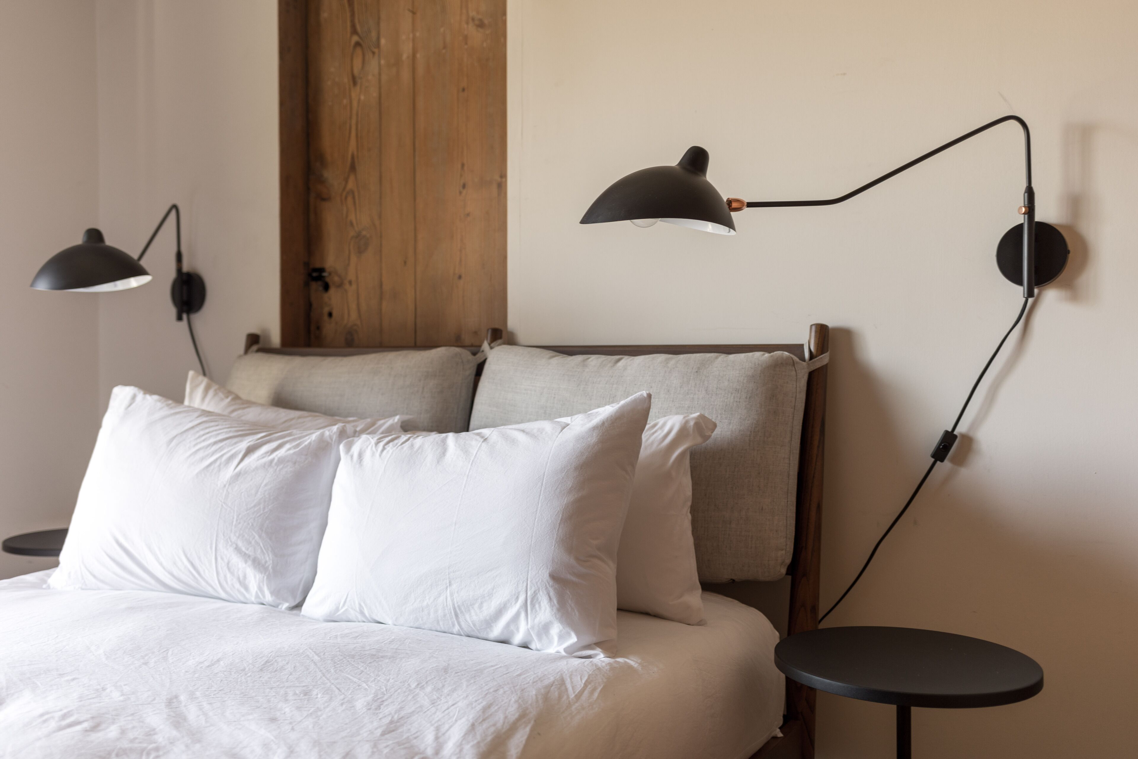 A neatly made bed with white linens and two pillows, a wooden headboard, and two black floor lamps on either side.