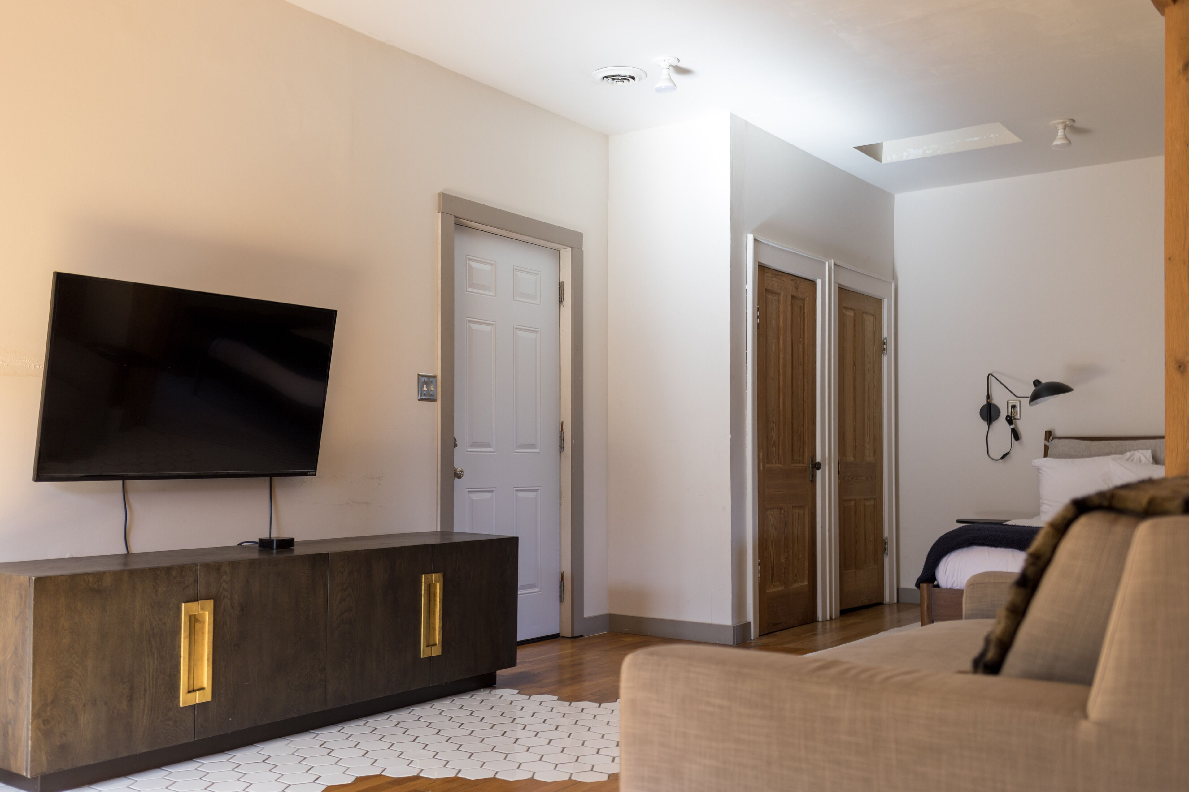 Un salon moderne avec un téléviseur à écran plat, un meuble en bois foncé, un canapé beige et un tapis à motifs.