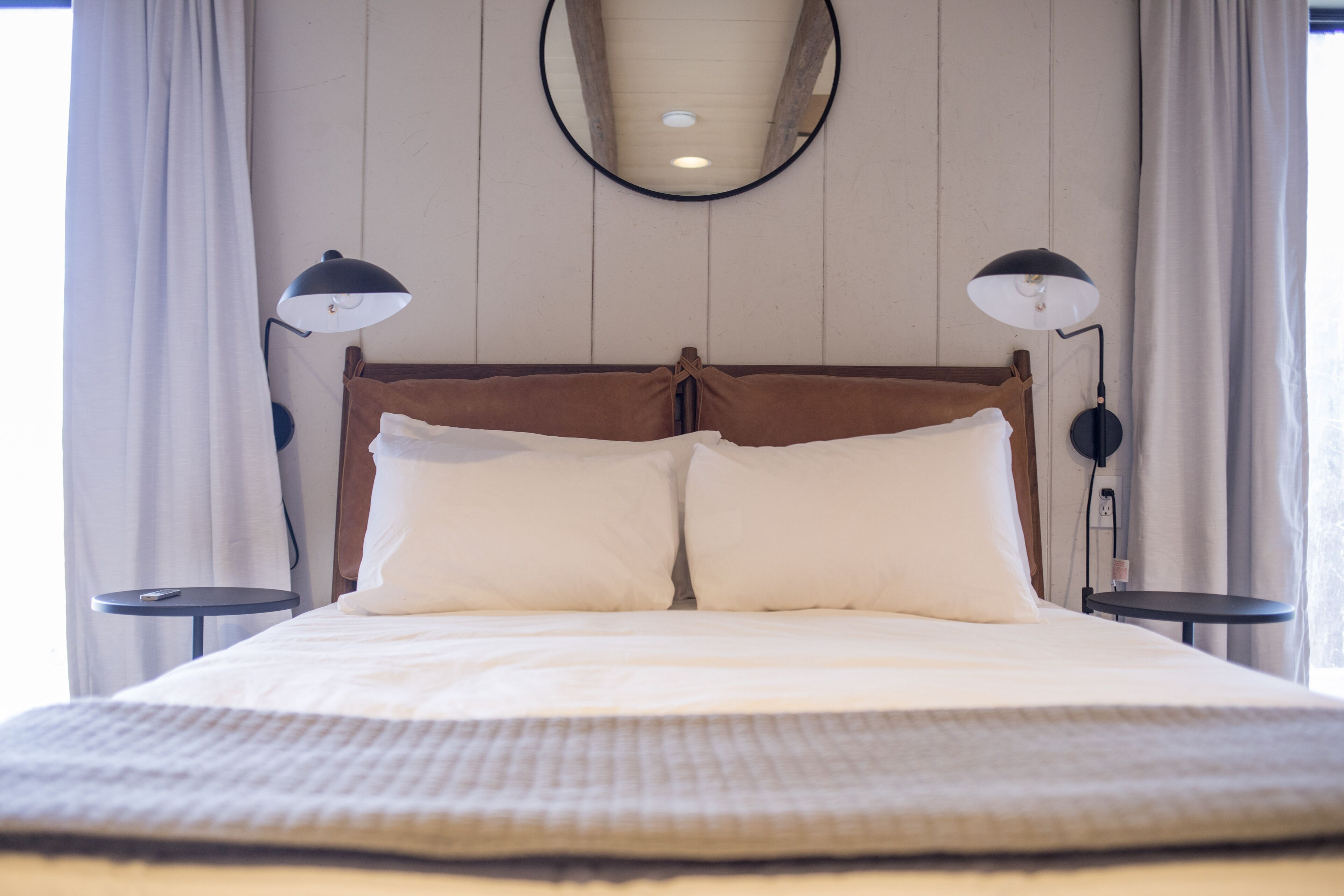 Un lit bien fait, avec une tête de lit en bois, deux tables de chevet avec des lampes et un miroir rond accroché au mur.