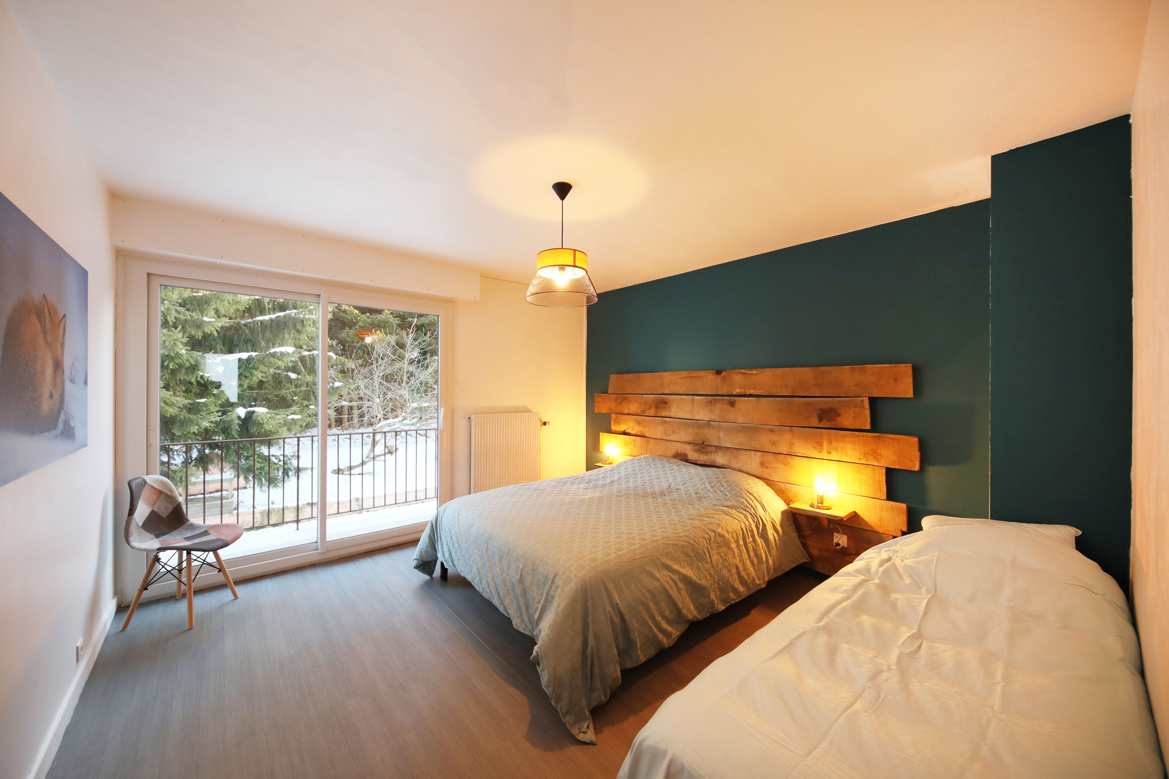 A bedroom with a large window, a wooden headboard, and a chair.