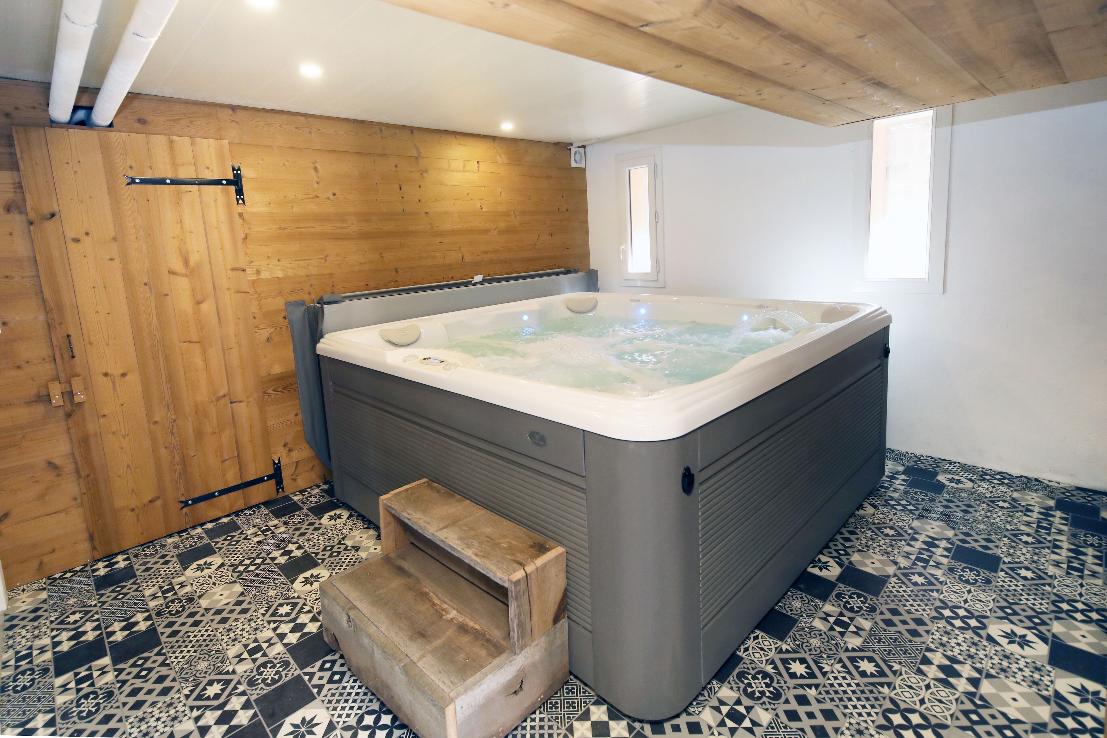 A hot tub in a room with wooden walls and patterned floor tiles.