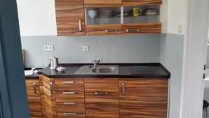 A kitchen with wooden cabinets, a black countertop, a stainless steel sink, and a coffee maker. - Renovated farmhouse in the northern Uckermark, between lakes and forests (Brüssow)