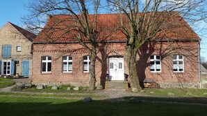 A traditional brick building with a red-tiled roof, large windows, and a prominent tree in front. - Renovated farmhouse in the northern Uckermark, between lakes and forests (Brüssow)