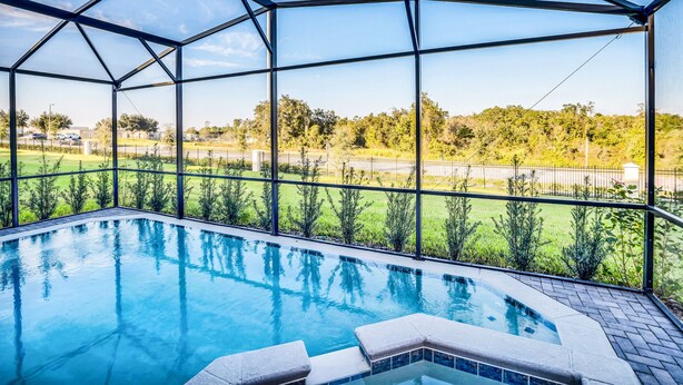 Ein Schwimmbecken mit Glasveranda, umgeben von einer gepflasterten Terrasse und Blick auf eine grüne Landschaft.