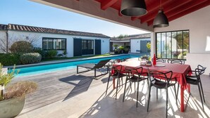 Portico coperto con piscina, zona pranzo all'aperto e vista su una casa moderna.
