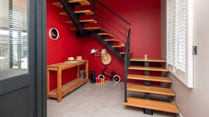 Un interno moderno con una parete rossa, una scala in legno, un tavolino con cappelli e una bicicletta.