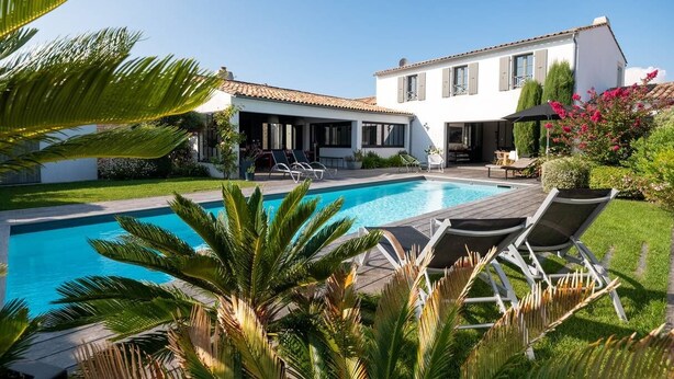 Una casa moderna con piscina, area relax esterna e vegetazione rigogliosa.
