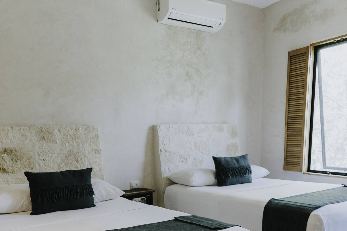 A room with two beds, a bench, a nightstand, and a window with shutters.