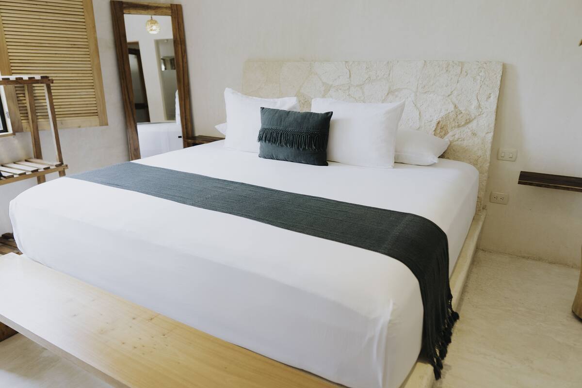 A neatly made bed with white and dark gray bedding, a stone-textured headboard, and a wooden bench at the foot of the bed.