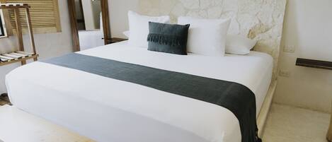 A neatly made bed with white linens and a green throw blanket, a wooden headboard, and a bedside table with a lamp.