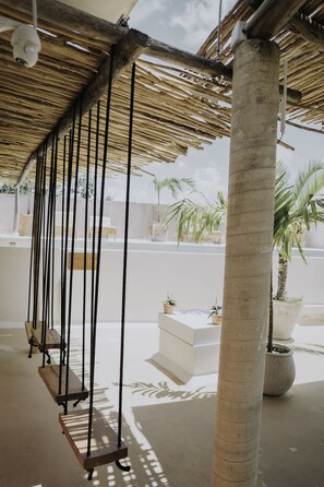A covered outdoor area with a thatched roof, wooden swings, and potted plants. - Koos Hotel Boutique Tulum (Tulum)