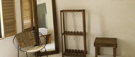 A bedroom with a bed, a chair, a mirror, and a shelf.