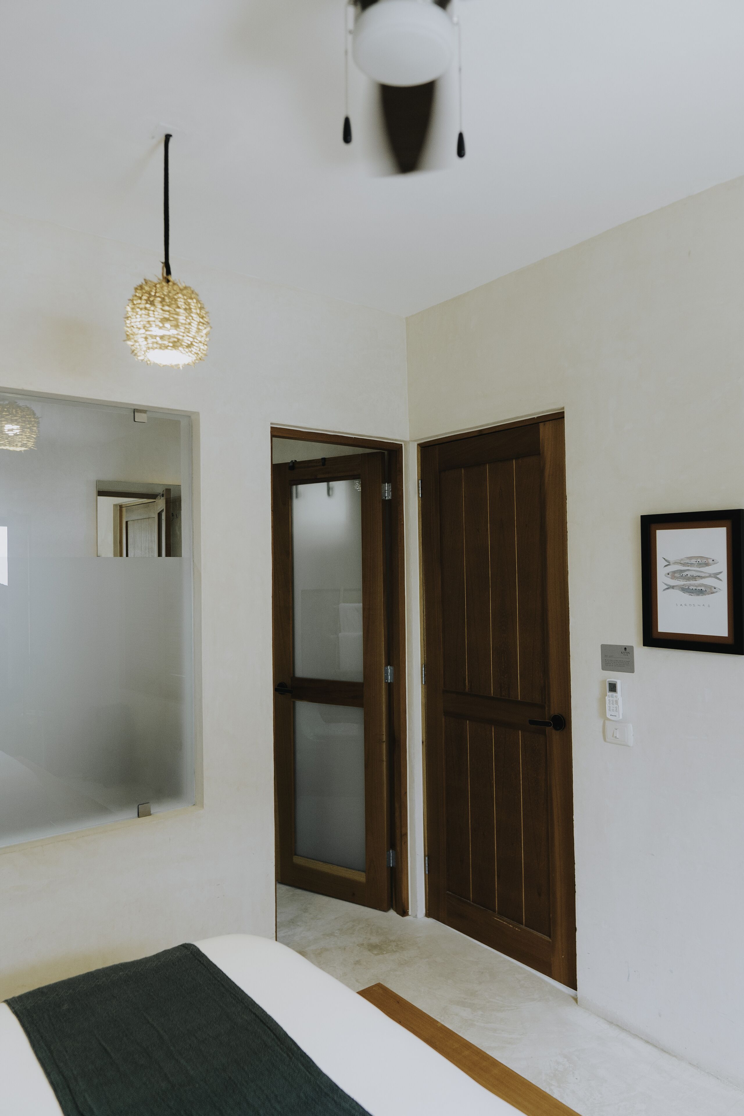 A bedroom with a bed, a hanging light fixture, a wooden door, and a framed picture on the wall.