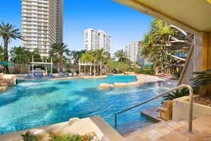 A resort pool area with clear blue water, palm trees, and high-rise buildings in the background. - Resort style 3br 2.5 bath w/huge entertainers balcony (Surfers Paradise)