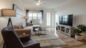 Ein Wohnzimmer mit Sofa, Sessel, Couchtisch, Fernseher und Deckenventilator.