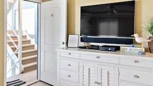 Ein Hotelzimmer mit einem großen Flachbildfernseher, einer weißen Kommode mit Schubladen, einem gerahmten Bild an der Wand und einer Treppe, die zu einem Außenbereich führt.