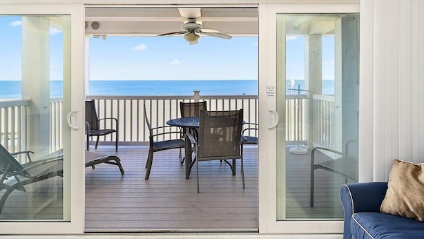 Ein Balkon mit Tisch und Stühlen, einem Deckenventilator und Blick auf das Meer.