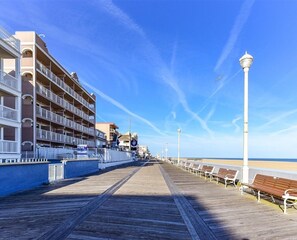 A wooden boardwalk with benches, a beach, and a hotel with balconies and railings. - The best of the best, 2BD direct Ocean Front with wide big ocean front  balcony . Relax and enjoy the ocean and the sun. (Ocean City)