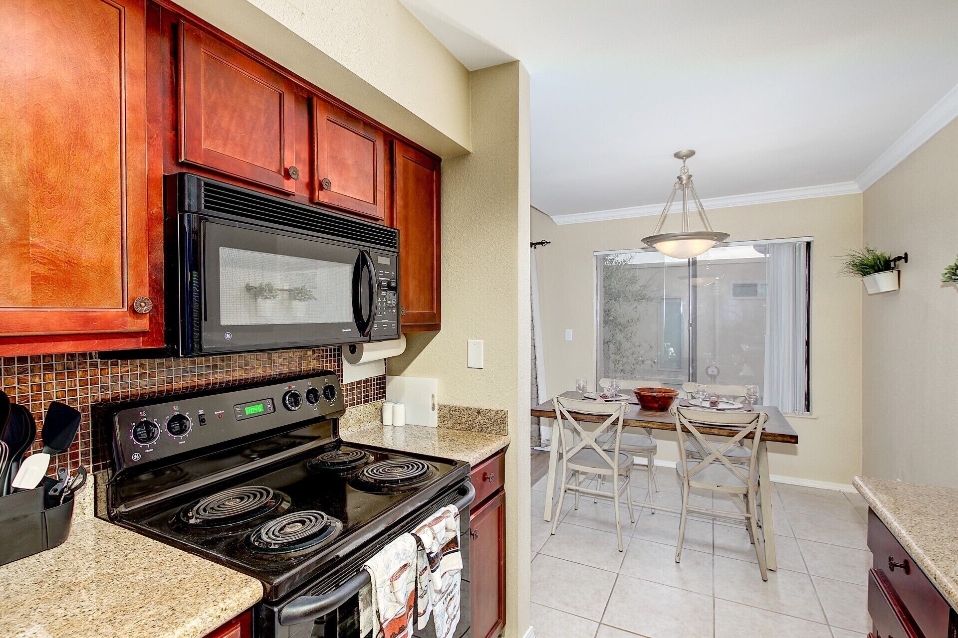 A kitchen with a stove, microwave, and cabinets. There is a dining area with a table and chairs.