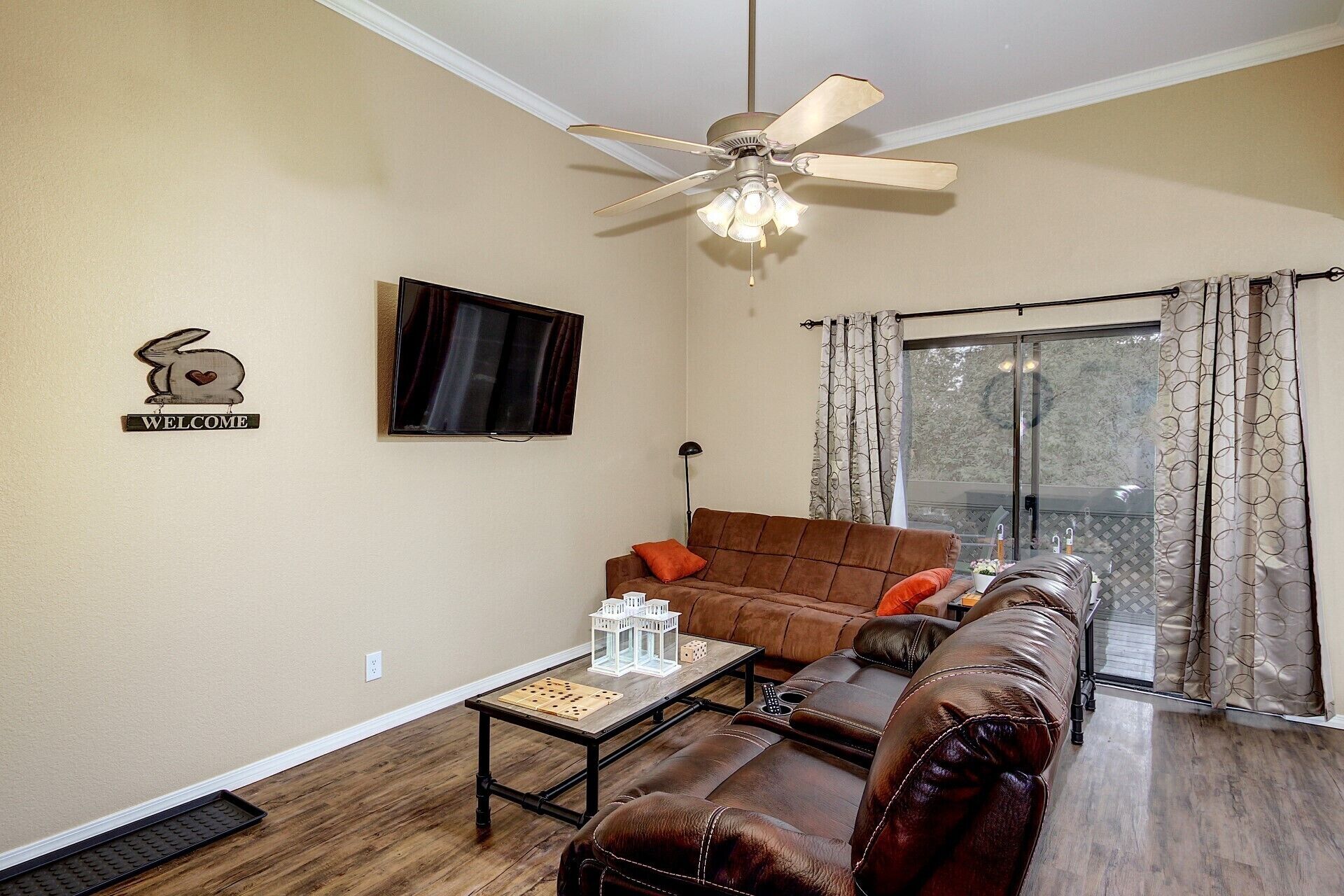 A living room with a brown leather sofa, a coffee table, a television, and a ceiling fan.