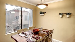 Un coin repas avec une table en bois dressée pour quatre personnes, un luminaire suspendu et deux jardinières fixées au mur.