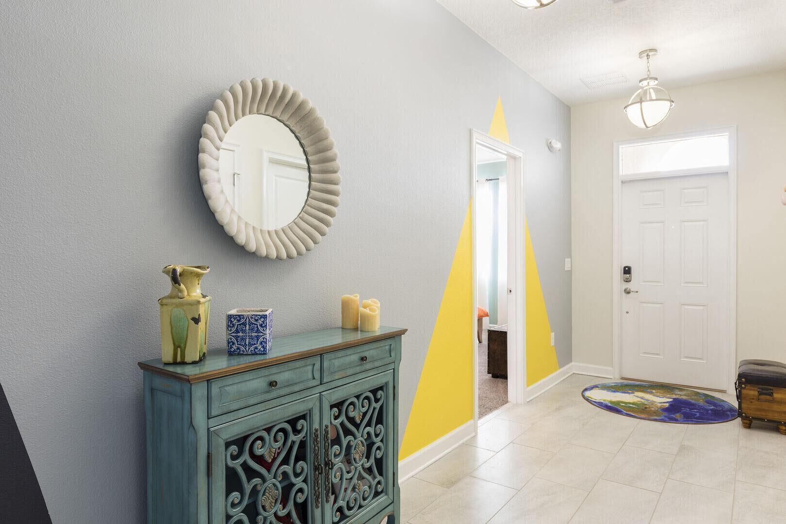 A hallway with a decorative mirror, a cabinet with items, and a door.