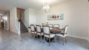A dining area with a wooden table and chairs, a chandelier, and a staircase in the background. - C9052sid- The Retreat at Champions Gate (Davenport)