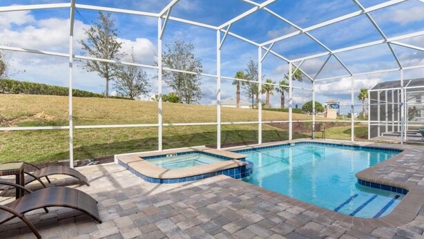 A covered outdoor swimming pool with a hot tub, surrounded by a white metal frame and a brick patio. - C9052sid- The Retreat at Champions Gate (Davenport)